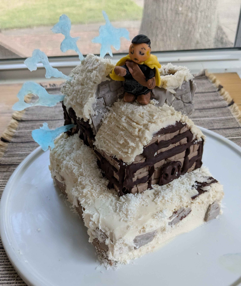 A cake in the shape of Goland Coal City from Final Fantasy Tactics. A tiny gumpaste Olan Durai chants, the glyphs for the Galaxy Stop spell in isomalt behind him.